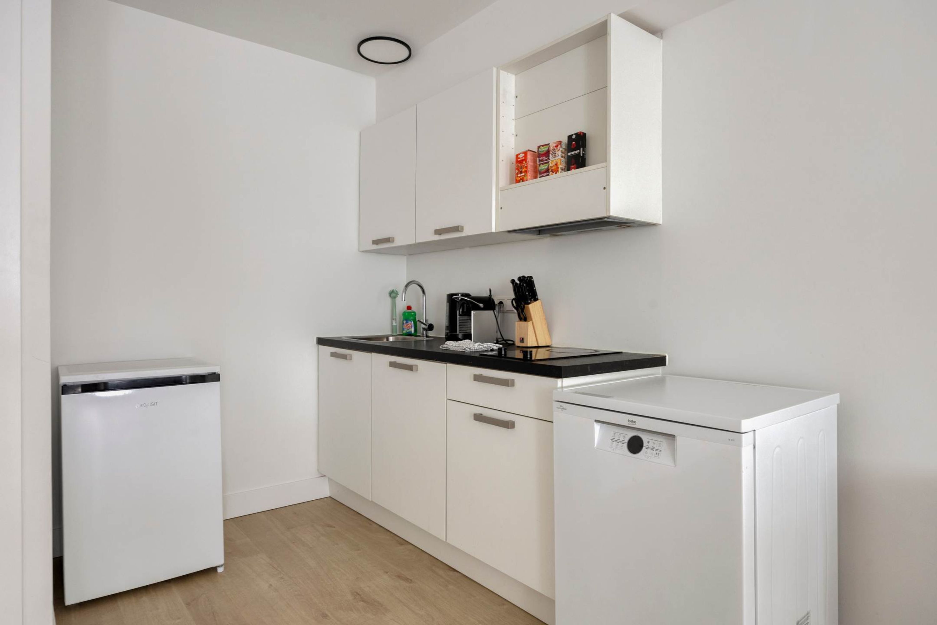 Una cocina compacta con armarios blancos, encimera negra y lavavajillas.