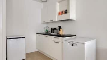 Una cocina compacta con armarios blancos, encimera negra y lavavajillas.