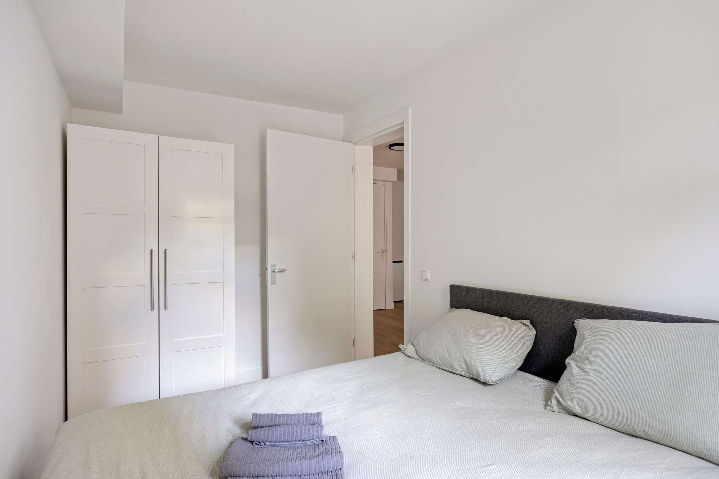Un dormitorio con cama, dos almohadas, una mesita de noche y un armario.