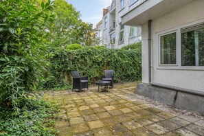 A courtyard with a paved patio, two wicker chairs, and dense greenery. - Stijlvol Comfortabel Appartement in het Hart van Rotterdam (Rotterdam)