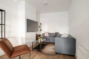 Ein modernes Wohnzimmer mit einer Couch, einem Glastisch, einem braunen Sessel und einem an der Wand befestigten Fernseher.