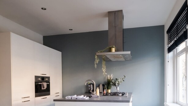 Una cocina moderna con armarios blancos, una isla central y una zona de comedor con mesa de madera y sillas verdes.