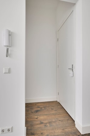 Ein Flur mit weißen Wänden, Holzboden, einer Tür, einem Lichtschalter und einem Telefon.
