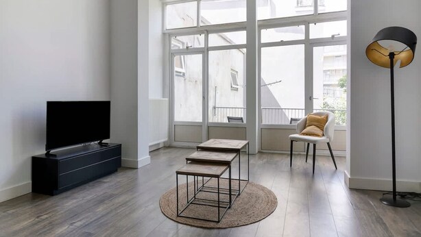A modern living room with a flat-screen TV, two wooden tables, a round rug, a white chair, and a floor lamp. - Bright Apartment With Private Terrace (Rotterdam)