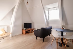 Ein Loft-Zimmer mit Fernseher, Esstisch mit Stühlen, einem Korbstuhl und einer Topfpflanze.