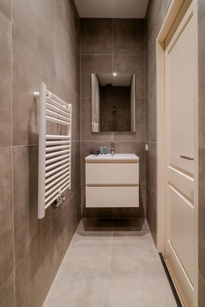Un baño estrecho con tocador blanco, un perchero y un espejo.