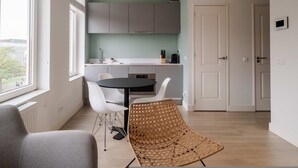 A modern kitchen with white cabinets, a dining table with chairs, and a wicker chair. - Cosy City Apartment in Rotterdam West (Rotterdam)