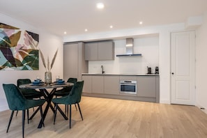 A modern kitchen with grey cabinets, a built-in oven, and a dining area with a round table and chairs. - Modern Ground-floor Apartment With Garden (Rotterdam)