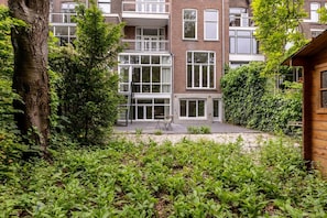 A multi-story residential building with a balcony, a paved courtyard, and dense greenery. - Modern Ground-floor Apartment With Garden (Rotterdam)