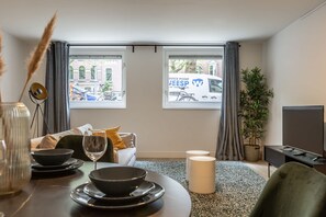 Uma sala de estar moderna com área de jantar, janelas amplas, um sofá, uma TV e um vaso com planta.