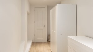 En smal gang med en hvid dør i enden, et hvidt skab og en hvid kommode.