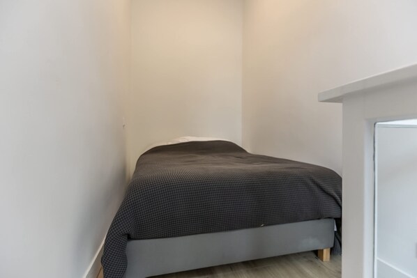A small, single-bed room with a grey bed, white walls, and a wooden floor. - Modern Lower-ground Apartment in Rotterdam West (Rotterdam)