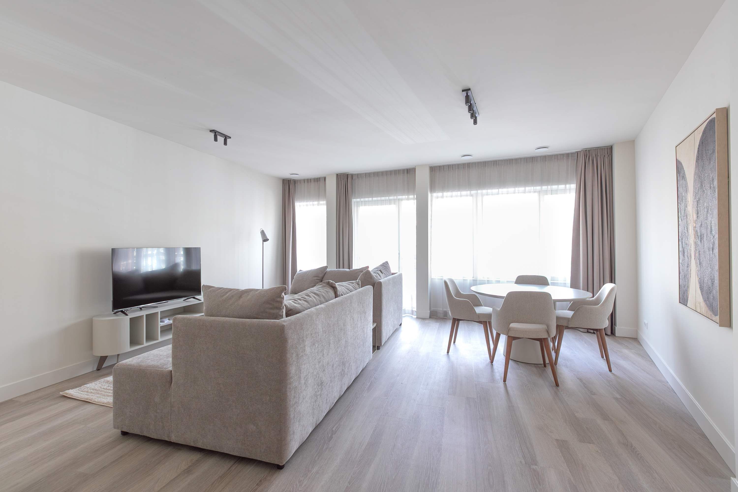 A modern living room with a sofa, TV, dining table, and chairs.