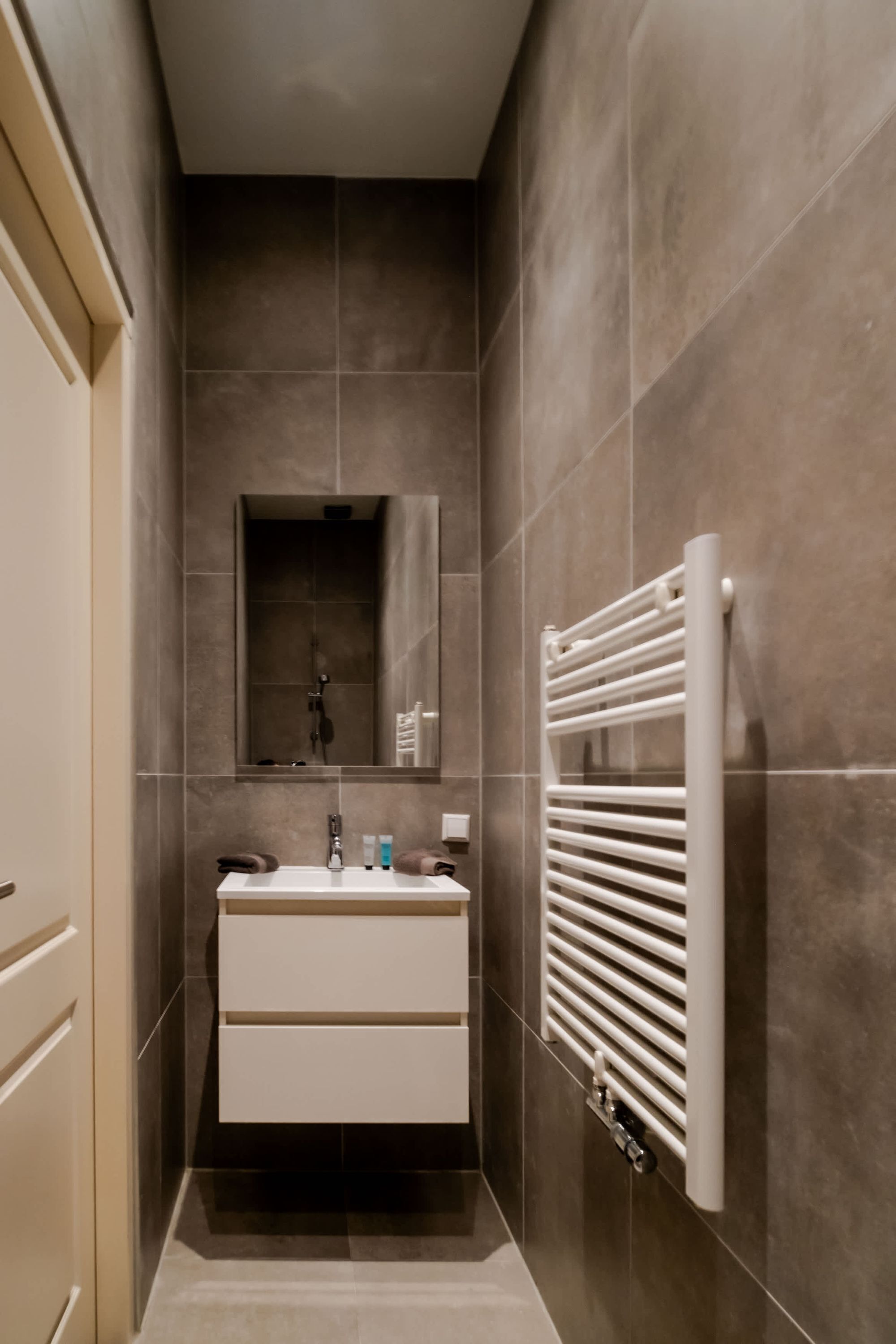 Een smalle badkamer met een wit wastafelmeubel, spiegel en handdoekhouder.