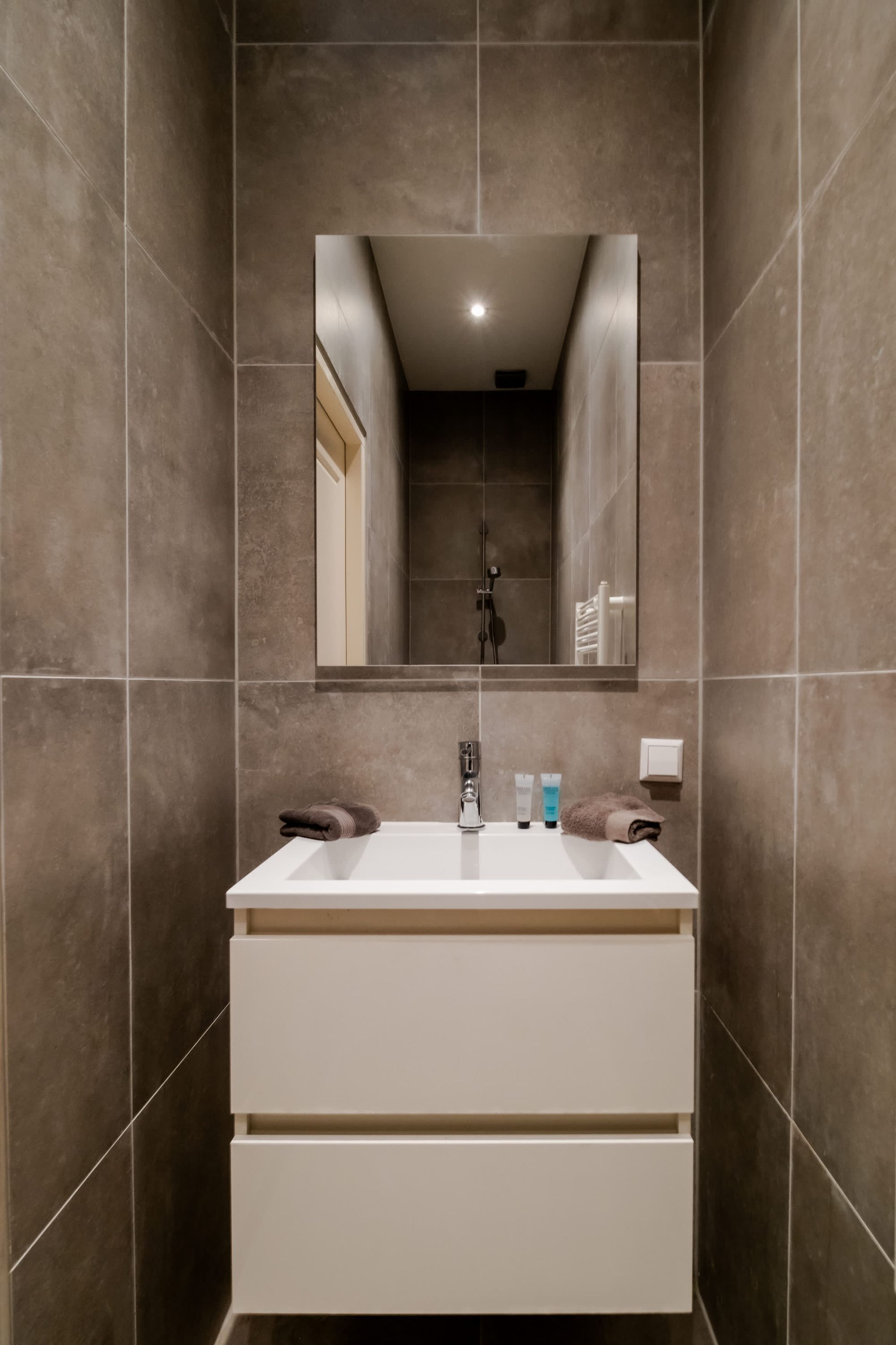 Een badkamer met een witte wastafel, spiegel en betegelde wanden.