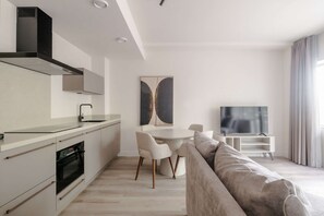 A modern kitchen with a built-in oven, a dining table with chairs, a flat-screen TV, and a large window with curtains.