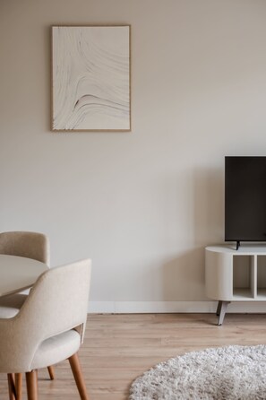 Ein minimalistisches Wohnzimmer mit einem modernen Sofa, einem Flachbildfernseher auf einem weißen Schrank und einem gerahmten abstrakten Gemälde an der Wand.
