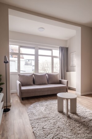 A modern living room with a sofa, a round coffee table, and a large window with curtains. - Modern Comfortable 1-bedroom Flat (Rotterdam)