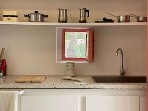 Eine Küche mit Fenster, Spüle, Schneidebrett und verschiedenen Töpfen im Regal.
