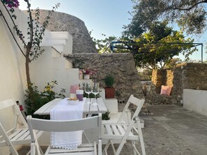 An outdoor dining area with a table set for two, surrounded by white chairs, a stone wall, and potted plants. - Le Liame di Anna 10 Minutes From the sea (Salve)