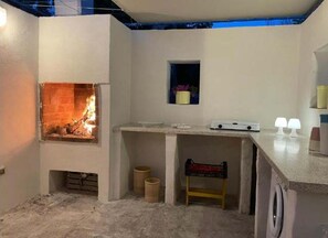 Ein Zimmer mit Kamin, einem kleinen Regal mit Topfpflanze, einem Holzstuhl und einer Anrichte mit zwei Lampen.