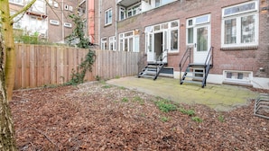 A brick building with a wooden fence, a staircase leading to a door, and a paved patio area. - Spacious Blijdorp Home With 4 Double Beds (Rotterdam)