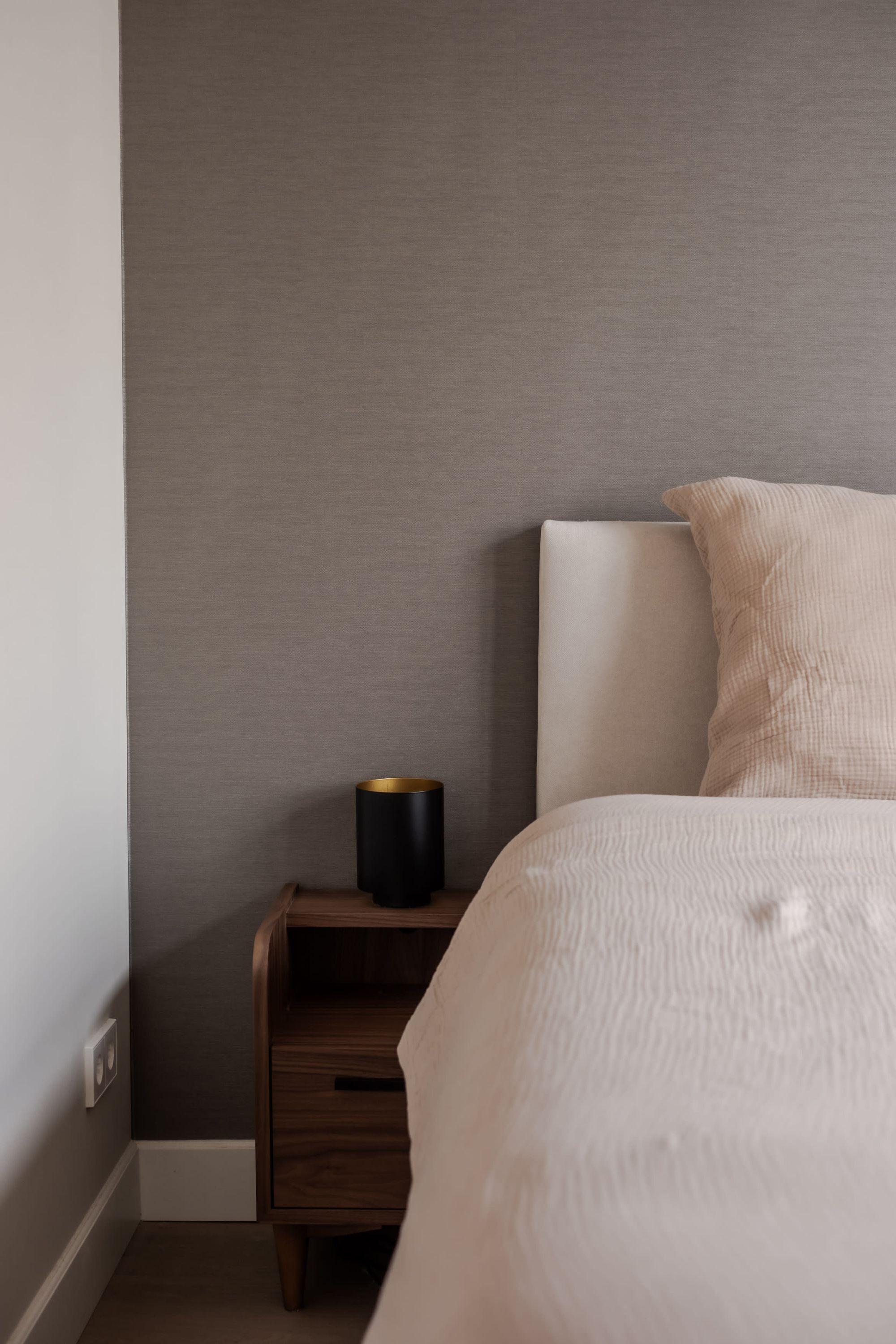 Un dormitorio con una cama, una mesita de noche y una lámpara de pared.