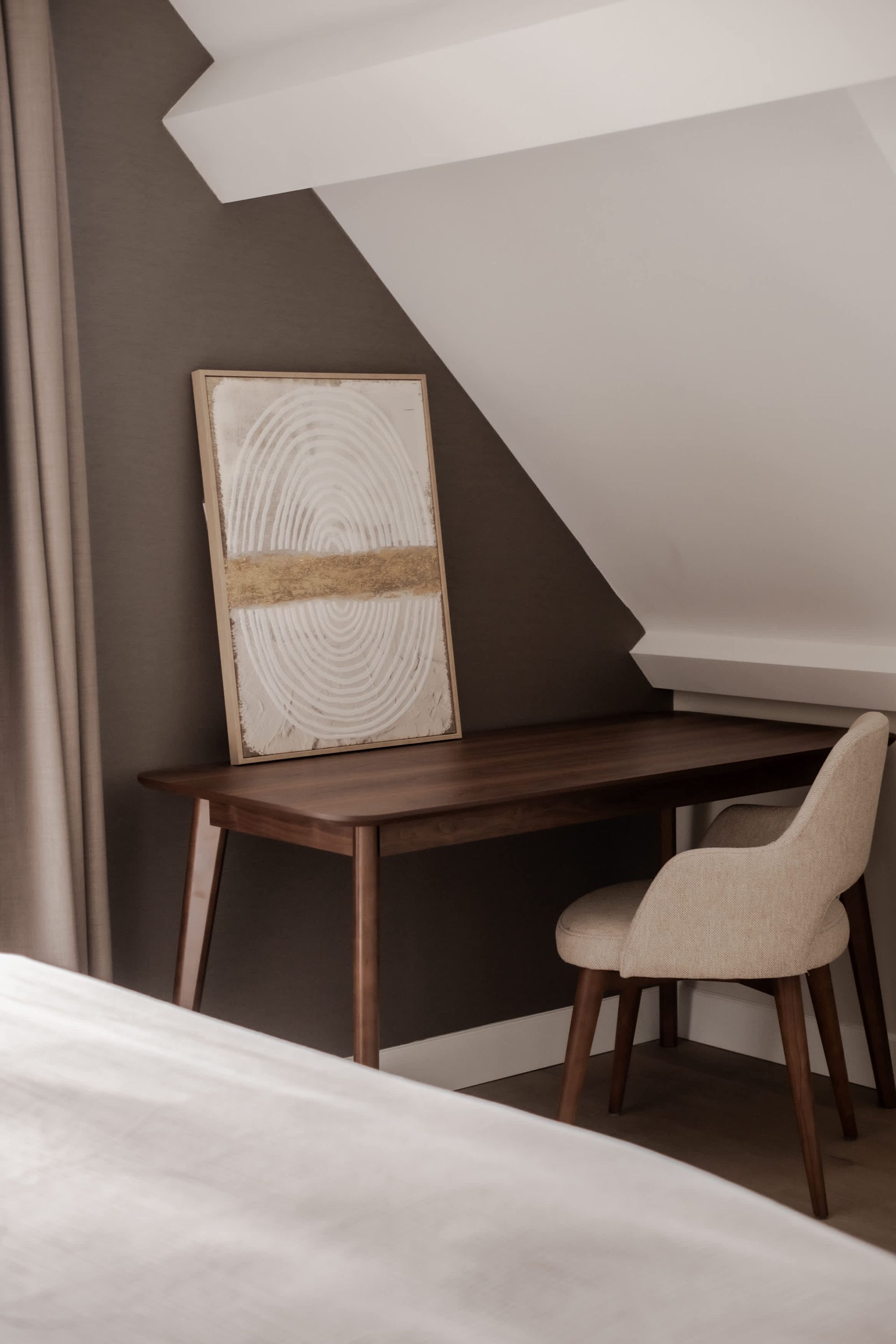 A modern room with a wooden desk, a chair, a framed artwork, and a sloped ceiling.