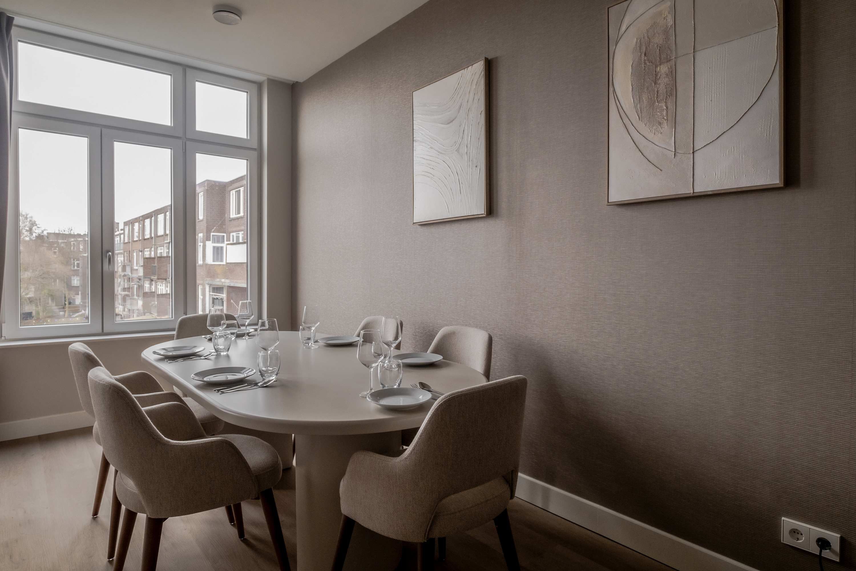 Un coin repas comprenant une table ronde, six chaises et une fenêtre donnant sur des immeubles.