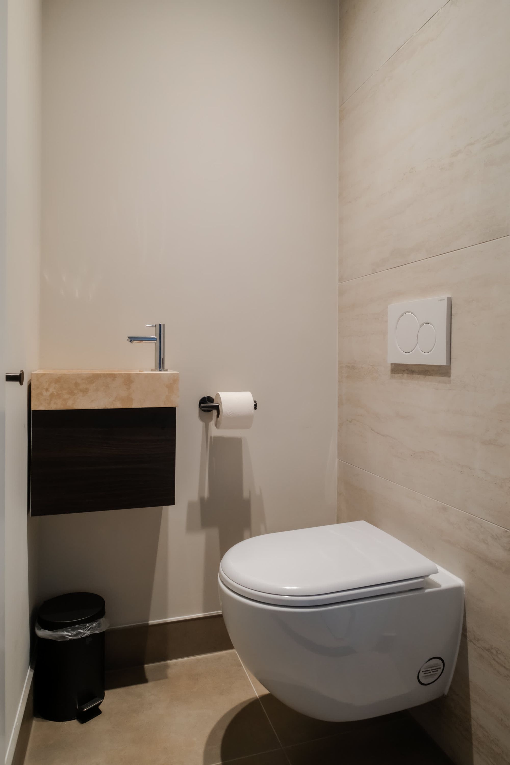 Et badeværelse med toilet, vask, skraldespand og et termostat på væggen.