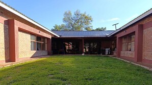 A building with a covered outdoor area, a grassy lawn, and brick walls. - Chiyedza Place (Juliasdale)