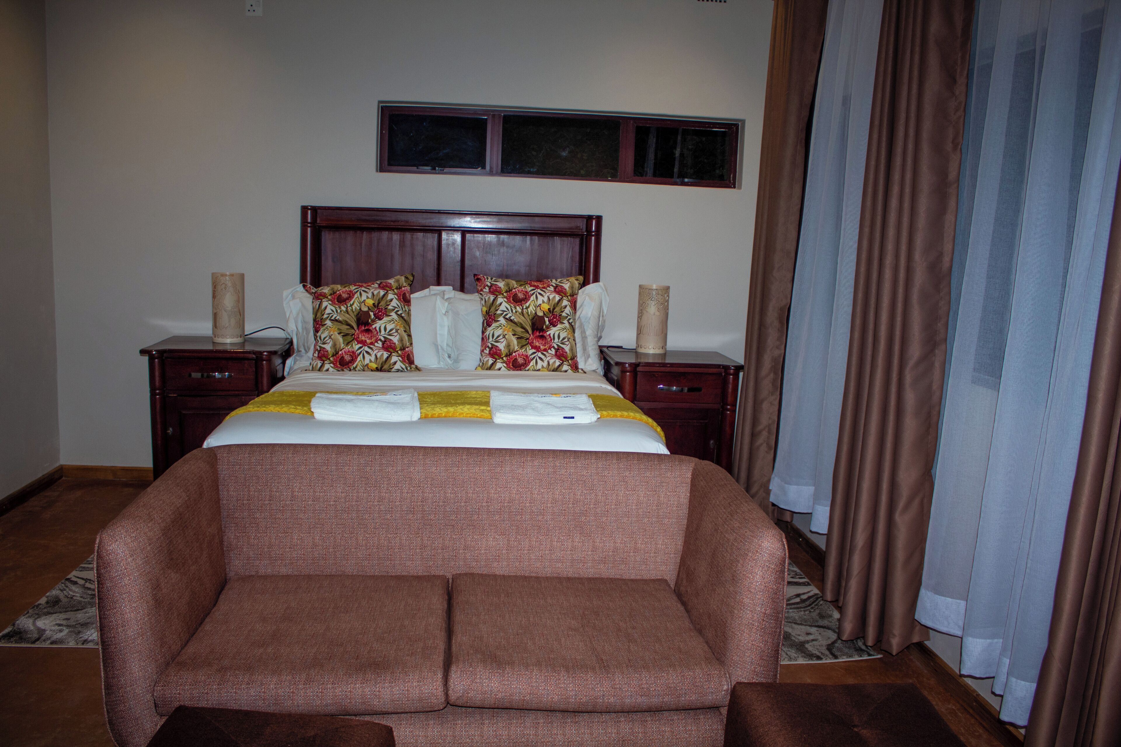 A hotel room with a bed, a sofa, a nightstand, a lamp, and a window with curtains.