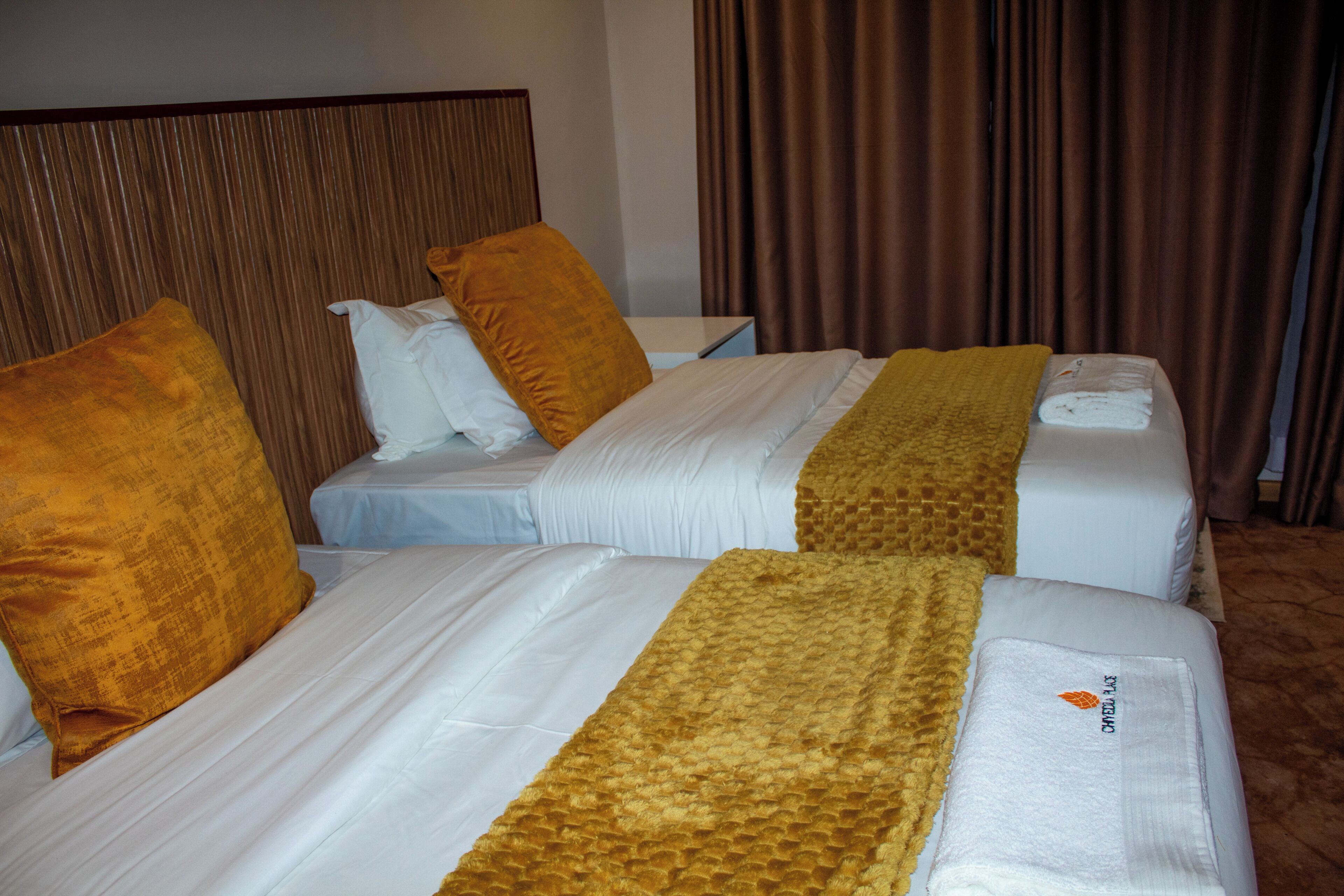 Quarto de hotel com duas camas, cada uma com colchão branco e manta marrom.