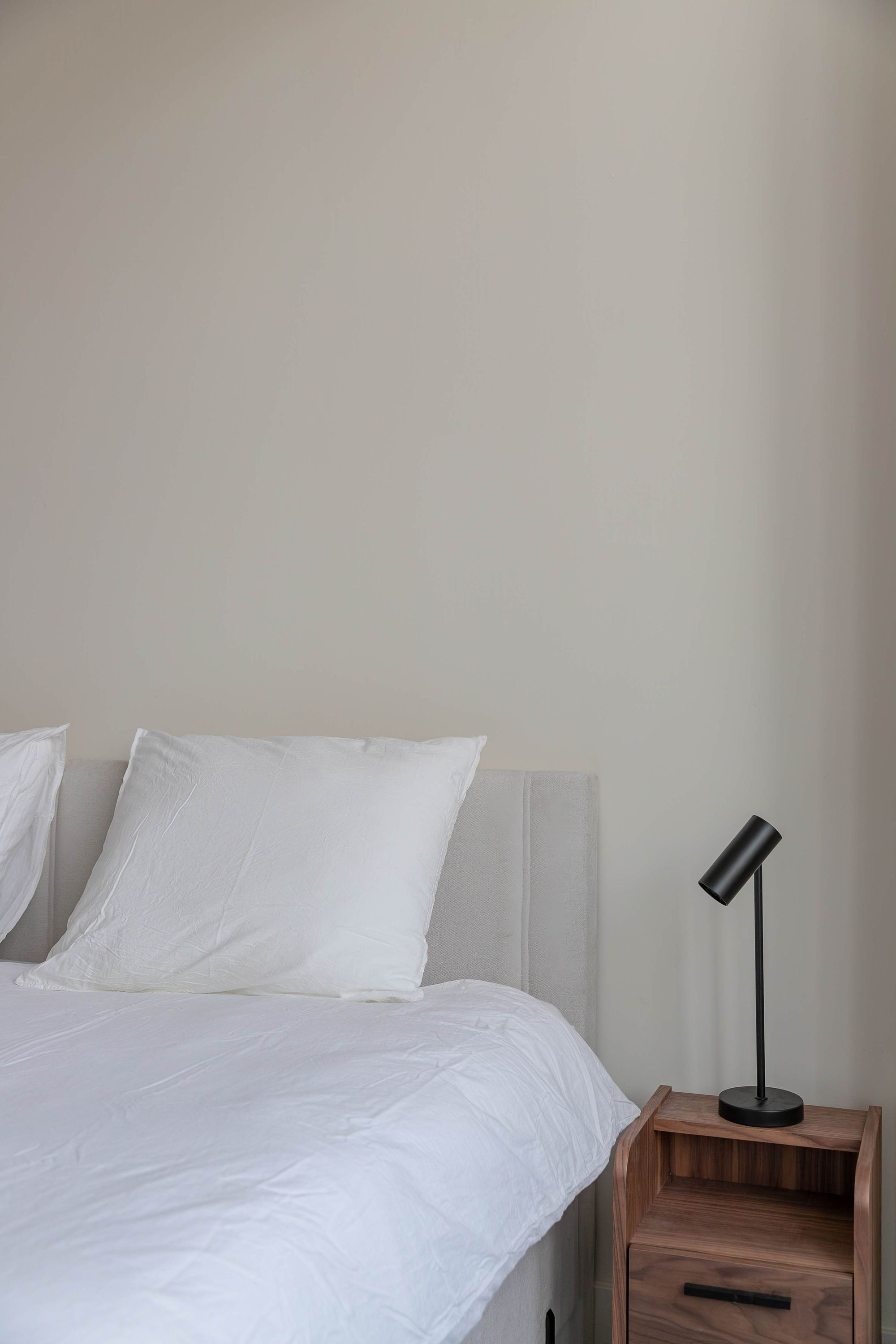 A bed with white bedding, a bedside table with a lamp, and a wooden nightstand drawer.