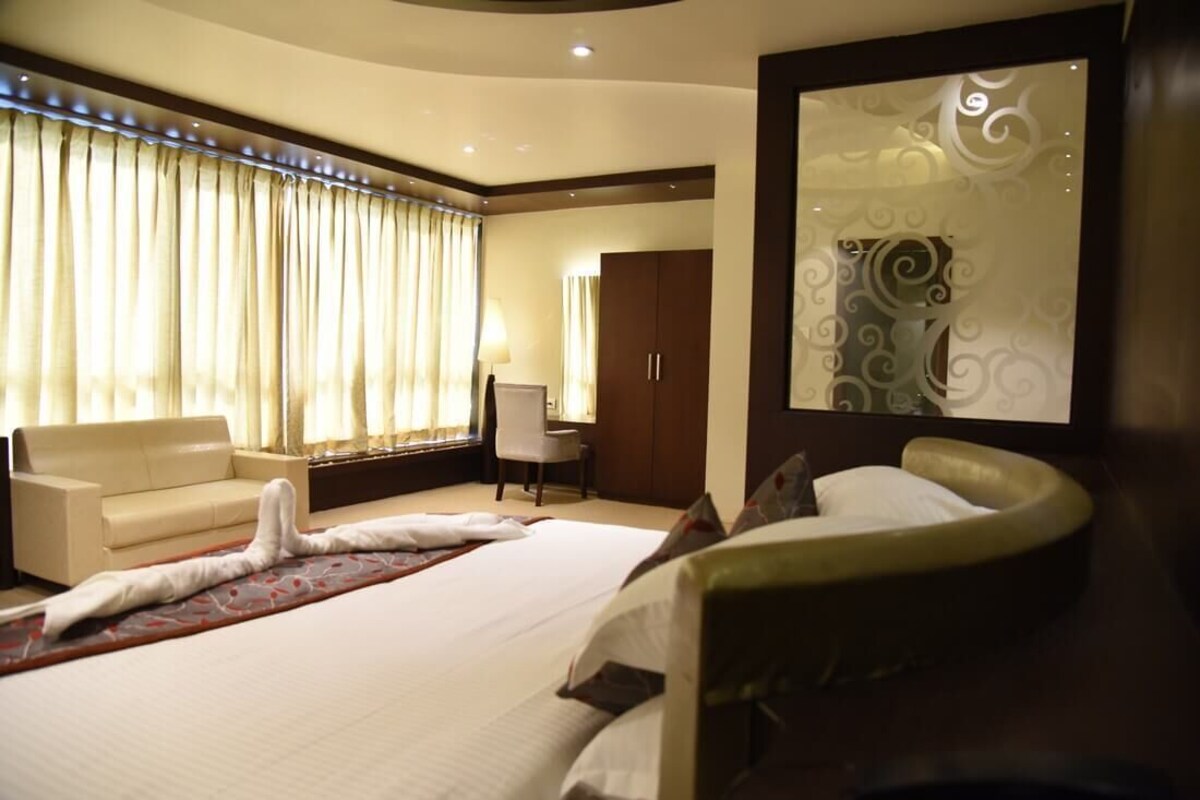 Quarto de hotel com cama grande, sofá, poltrona, escrivaninha e espelho.
