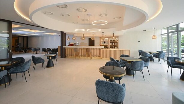 Un café moderno con mesas redondas, sillas azules, una zona de bar central y un diseño de techo circular.