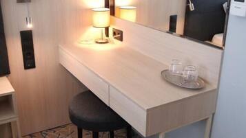A hotel room with a wooden desk, two wall-mounted lamps, a mirror, and a small stool.