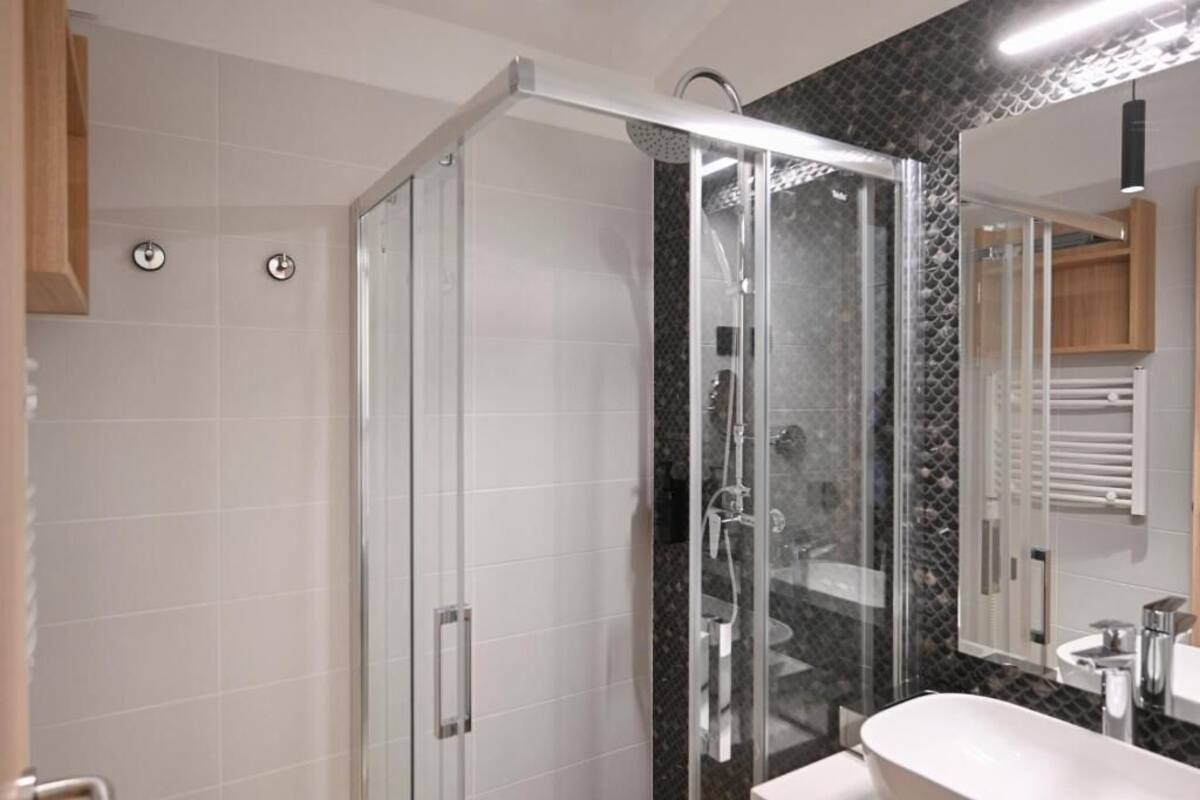 A modern bathroom with a glass-enclosed shower, a white sink, and a large mirror.