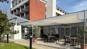 Un patio al aire libre con mesas y sillas, un área de estar cubierta y un edificio con fachada de ladrillo al fondo.