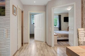 A hallway leading to a bedroom with a bed, a television, and a window with curtains. - Apartment '3 Ebenerdig' (Cuxhaven)