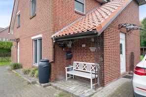 A brick building with a tiled roof, a bench, a trash bin, and a mailbox. - Apartment '3 Ebenerdig' (Cuxhaven)