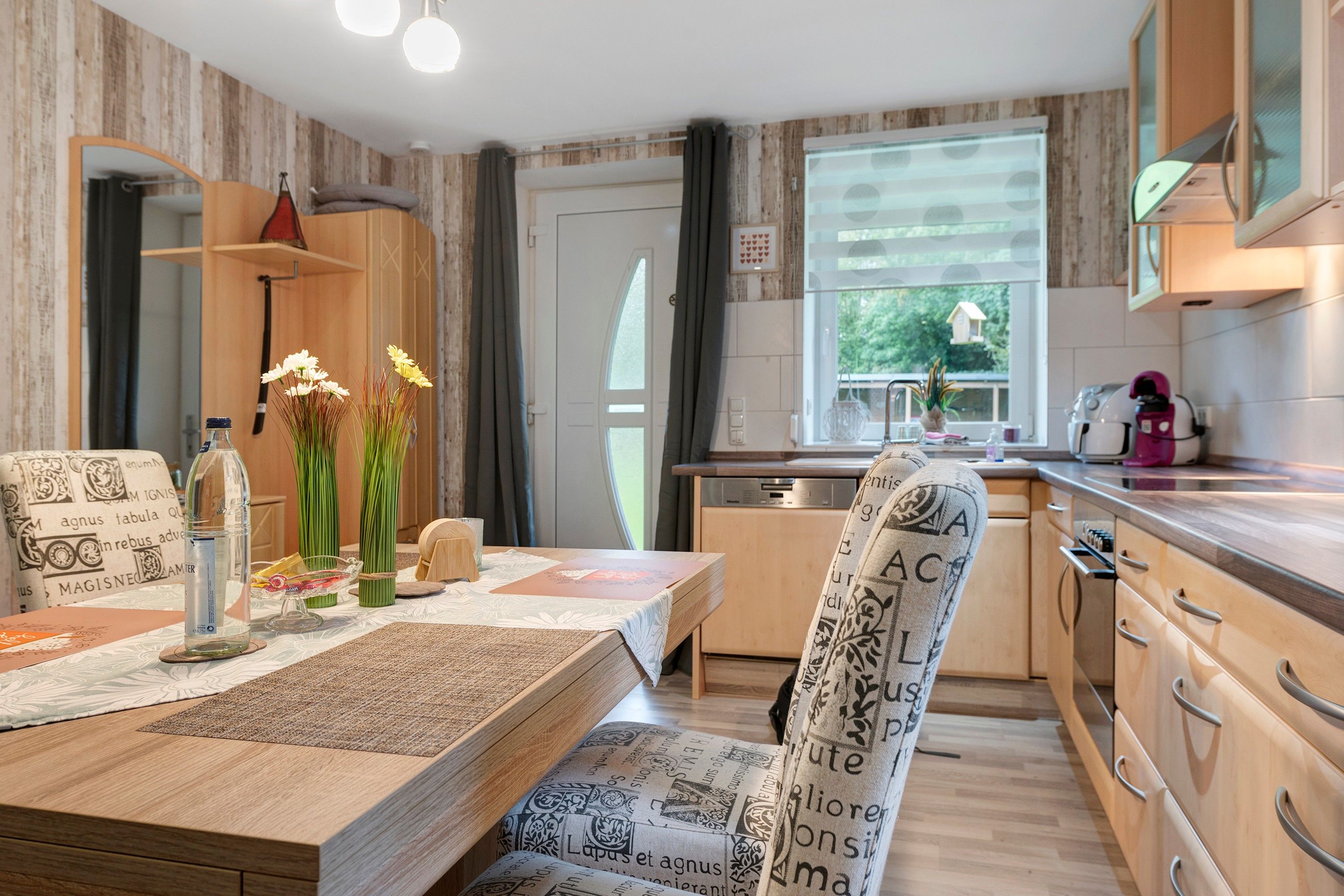 Eine moderne Küche mit Holzschränken, einem Esstisch mit gemustertem Tischläufer und einem Stuhl mit bedrucktem Design.