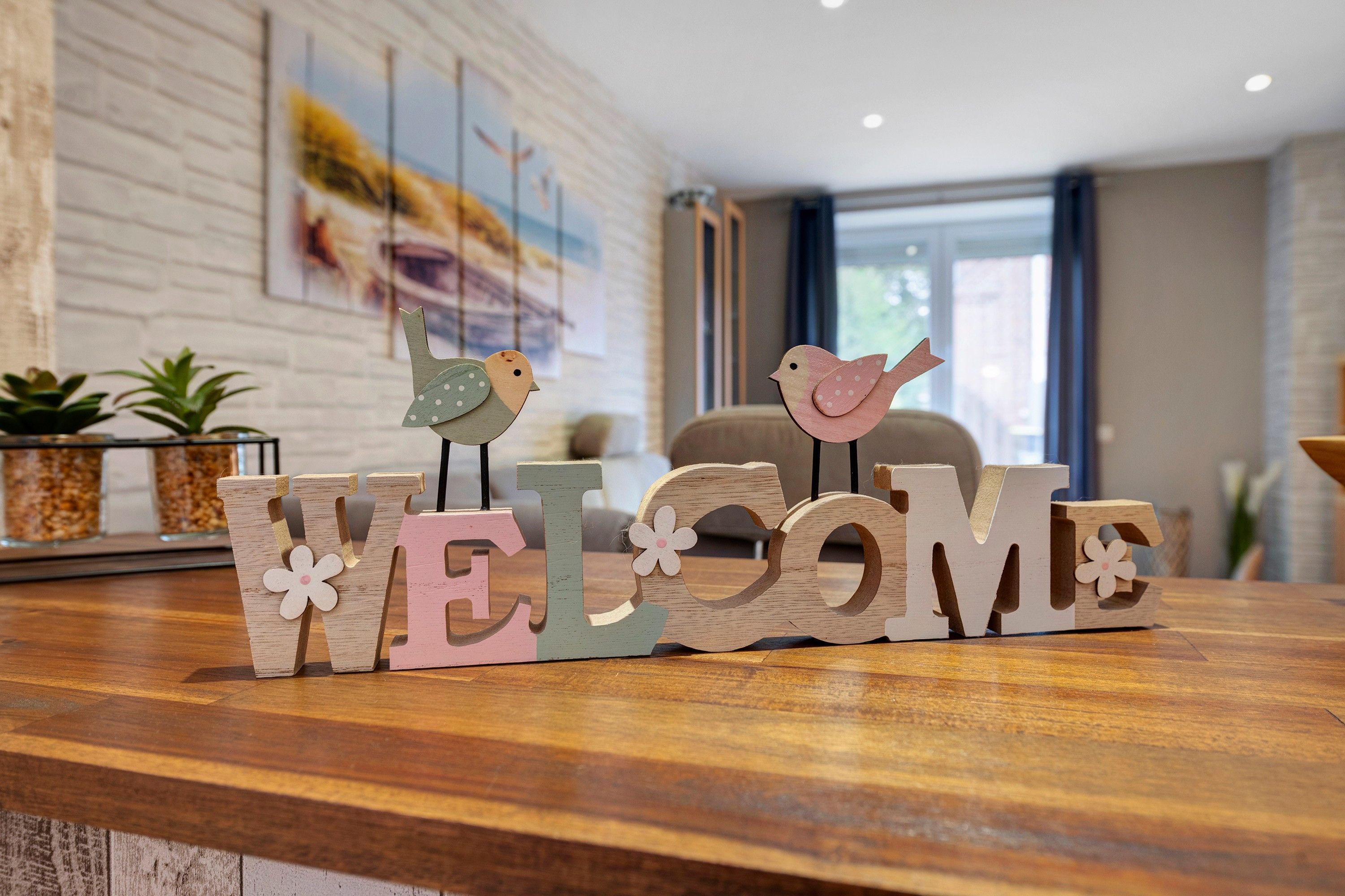 Ein Holzschild mit der Aufschrift 'WELCOME' und zwei Vogeldekorationen auf einer Holzunterlage.
