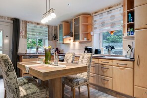 A modern kitchen with wooden cabinets, a dining table with chairs, and a view of the outdoors through large windows. - Apartment '3 Ebenerdig' (Cuxhaven)