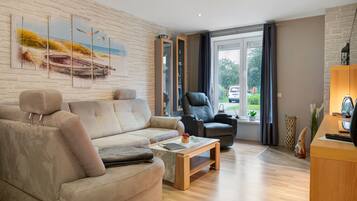 Ein modernes Wohnzimmer mit einem beige-farbenen Sofa, einem schwarzen Ledersessel, einem Holztisch und einem großen Fenster mit Vorhängen.