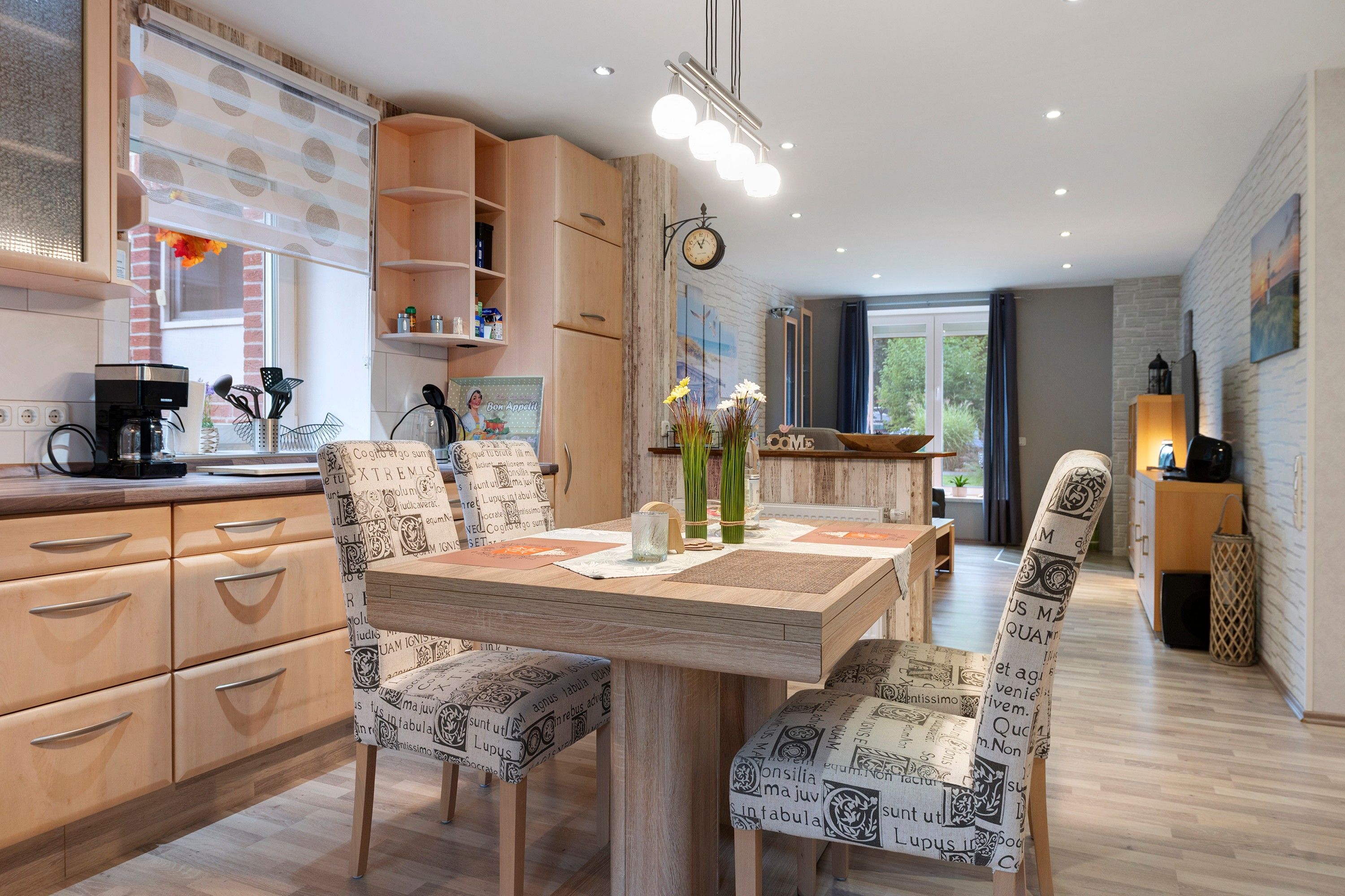 A modern kitchen with wooden cabinets, a coffee machine, and a dining area with patterned chairs and a table.