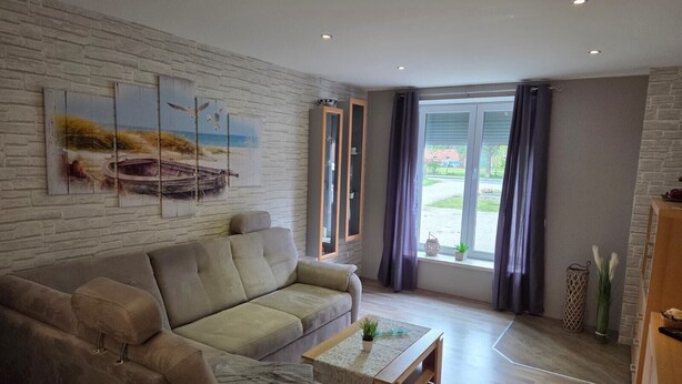 A living room with a sofa, a coffee table, and a view through a large window. - Apartment '3 Ebenerdig' (Cuxhaven)