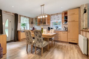 A modern kitchen with wooden cabinets, a dining table with patterned chairs, and a built-in oven. - Apartment '3 Ebenerdig' (Cuxhaven)