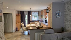 A modern kitchen with wooden cabinets, a dining table, and a clock on the wall. - Apartment '3 Ebenerdig' (Cuxhaven)