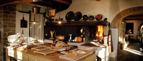Uma cozinha rústica com uma ilha grande, panelas penduradas e um forno de tijolos.